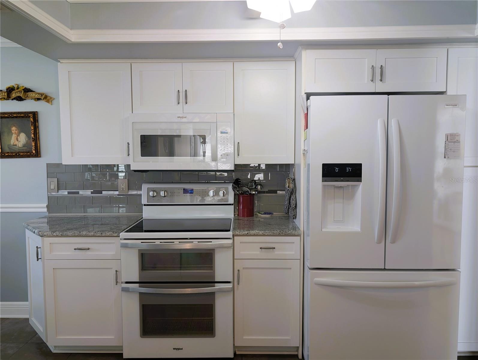 Updated white appliances include Frigidaire French door refrigerator with ice/water dispenser in door (2022), Whirlpool Gold glasstop range with double oven (2021) and matching WP microwave hood (2023). Pantry to right of refrigerator.