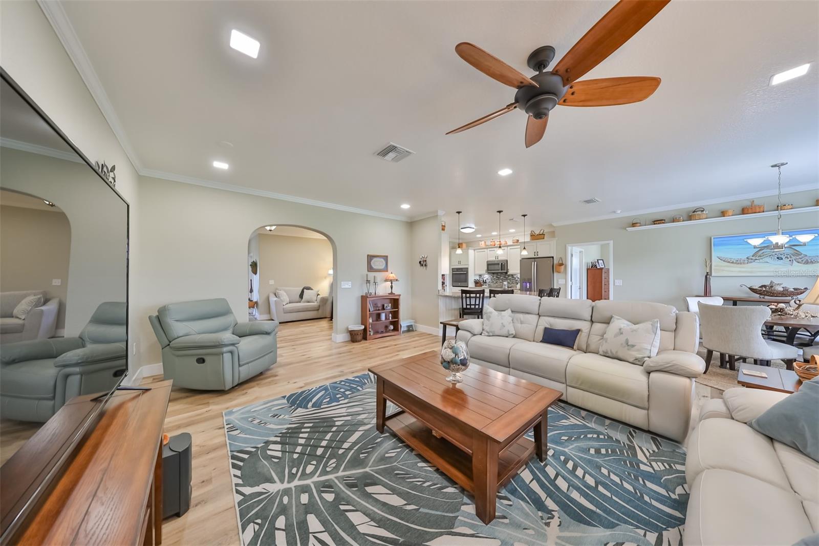 Arched entrance ways lead into the great room, kitchen, and dinette area. Notice the custom wall shelving, ceiling fan and updated recessed lighting extends throughout the entire spaces.