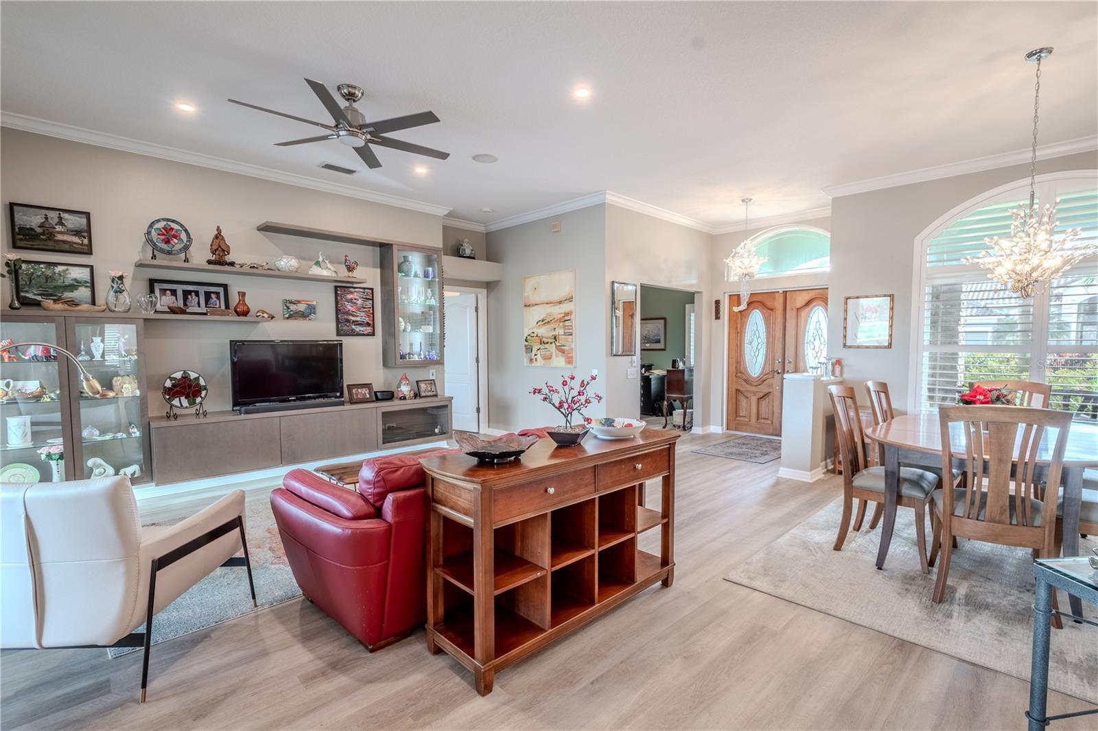 The living room features luxury vinyl plank flooring, a sleek, modern ceiling fan and a built in wall unit with led lighting.