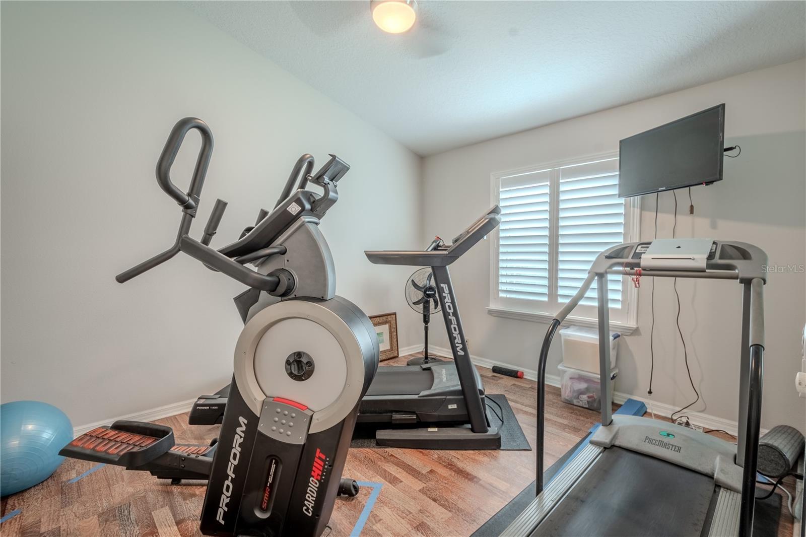 Bedroom 2 (currently serving as a home gym) features wood flooring, a built-in closet, a ceiling fan and shutters.