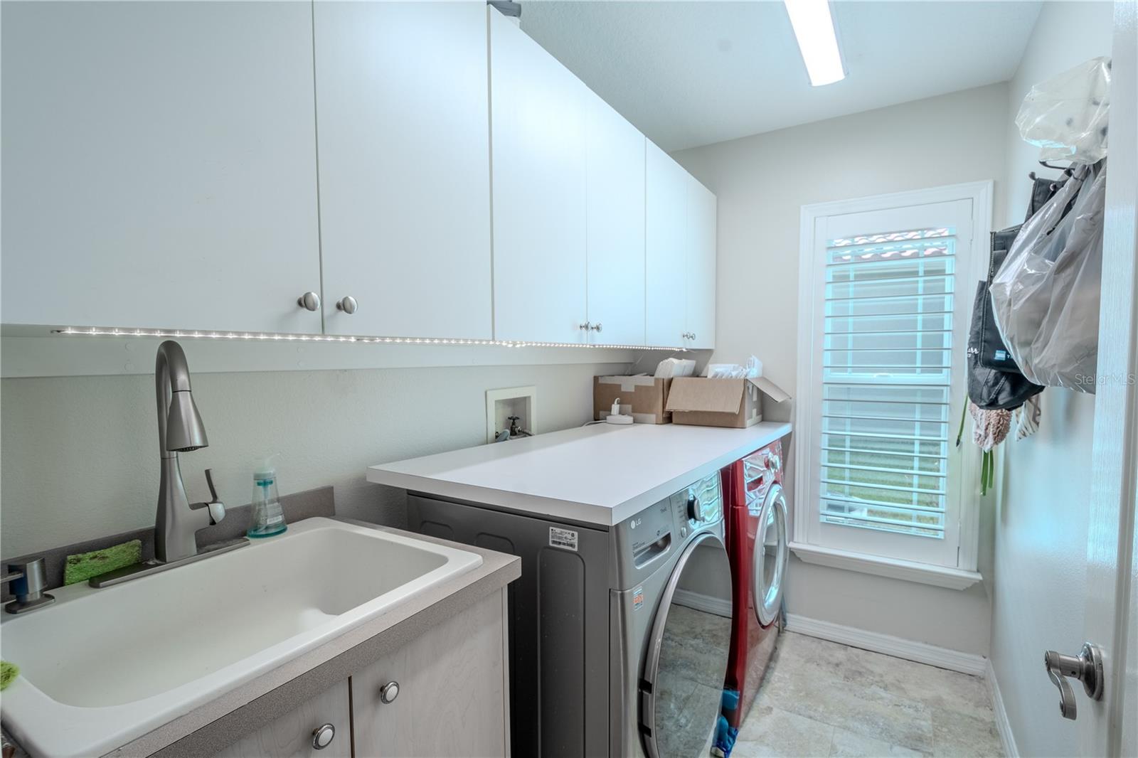 The laundry room has front load washer and dryer, a wall of built-in cabinets above and a utility sink with additional storage.