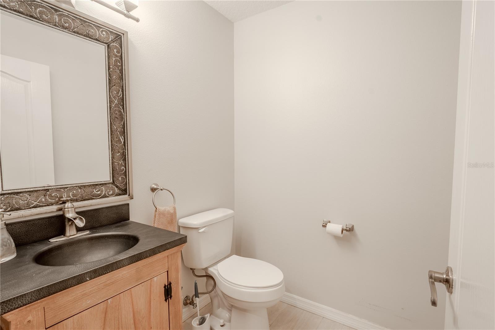 This half bath features a mirrored vanity with storage and light kit. It is upstairs adjacent to the bonus room.