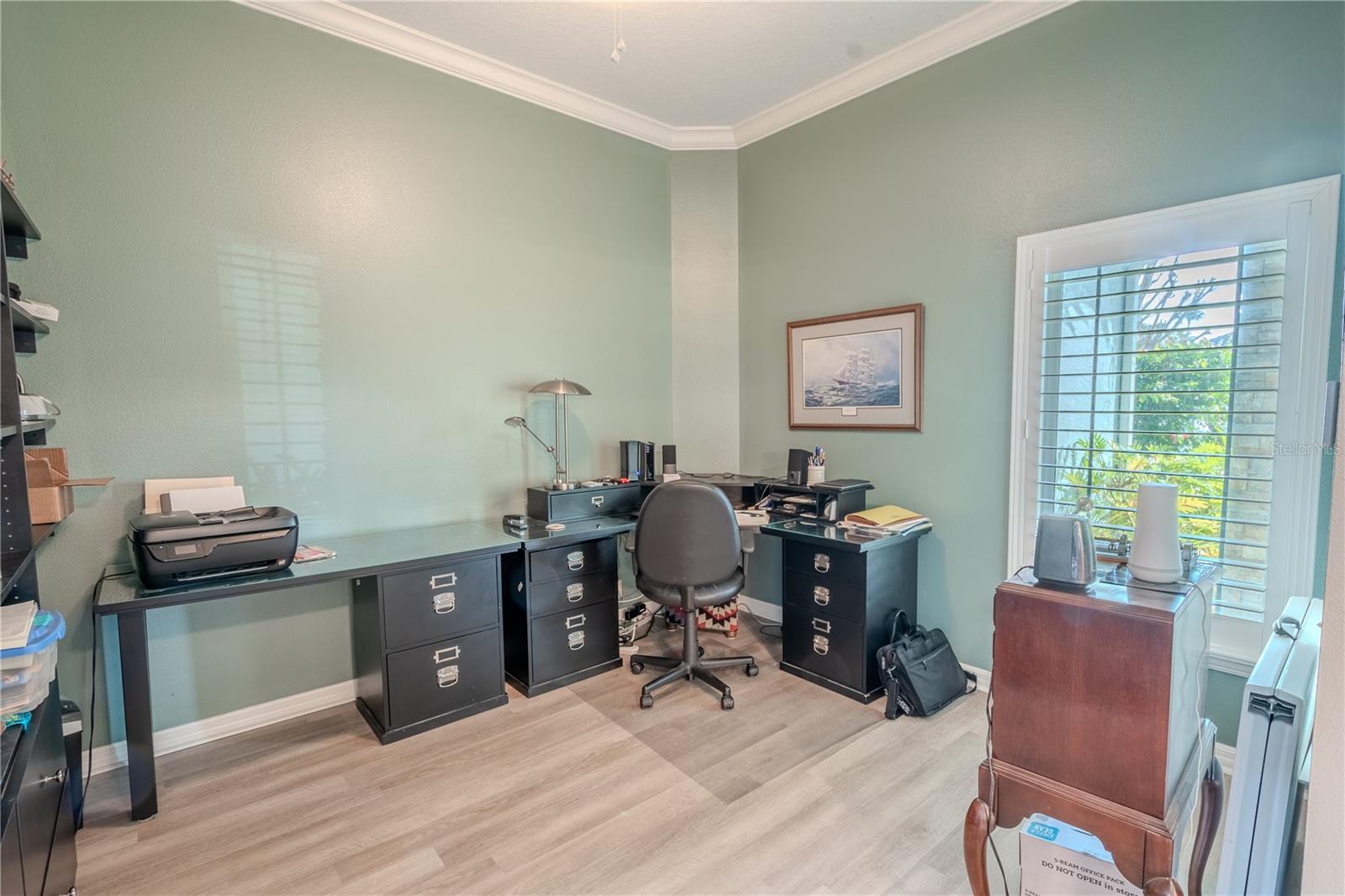 The home office/study features a built in wall unit, luxury vinyl plank flooring, shutters and crown molding.