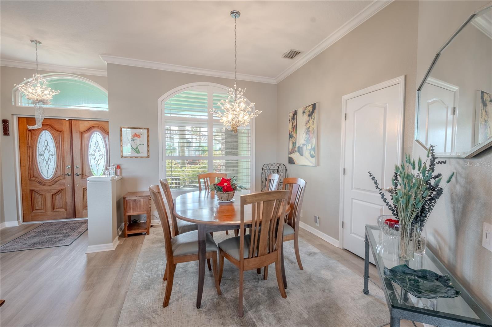 The dining room features an arched window with shutters, a refined chandelier that adds a touch of timeless elegance, crown molding and luxury vinyl plank flooring.