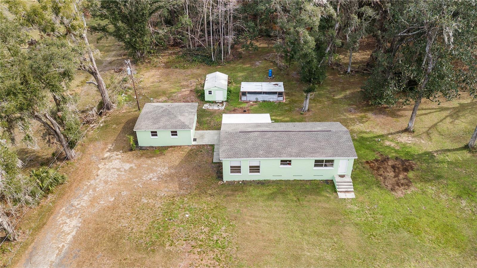 Ariel view of the serene 2.5 acre property with a 3/2 cement block one story home in an X flood Zone with a detached 2-car garage, and a storage shed, and an RV dumpstation.  Lined with trees for privacy. Surrounded by nature & one neighbor has a vast horse and cow pasture with acres of land.