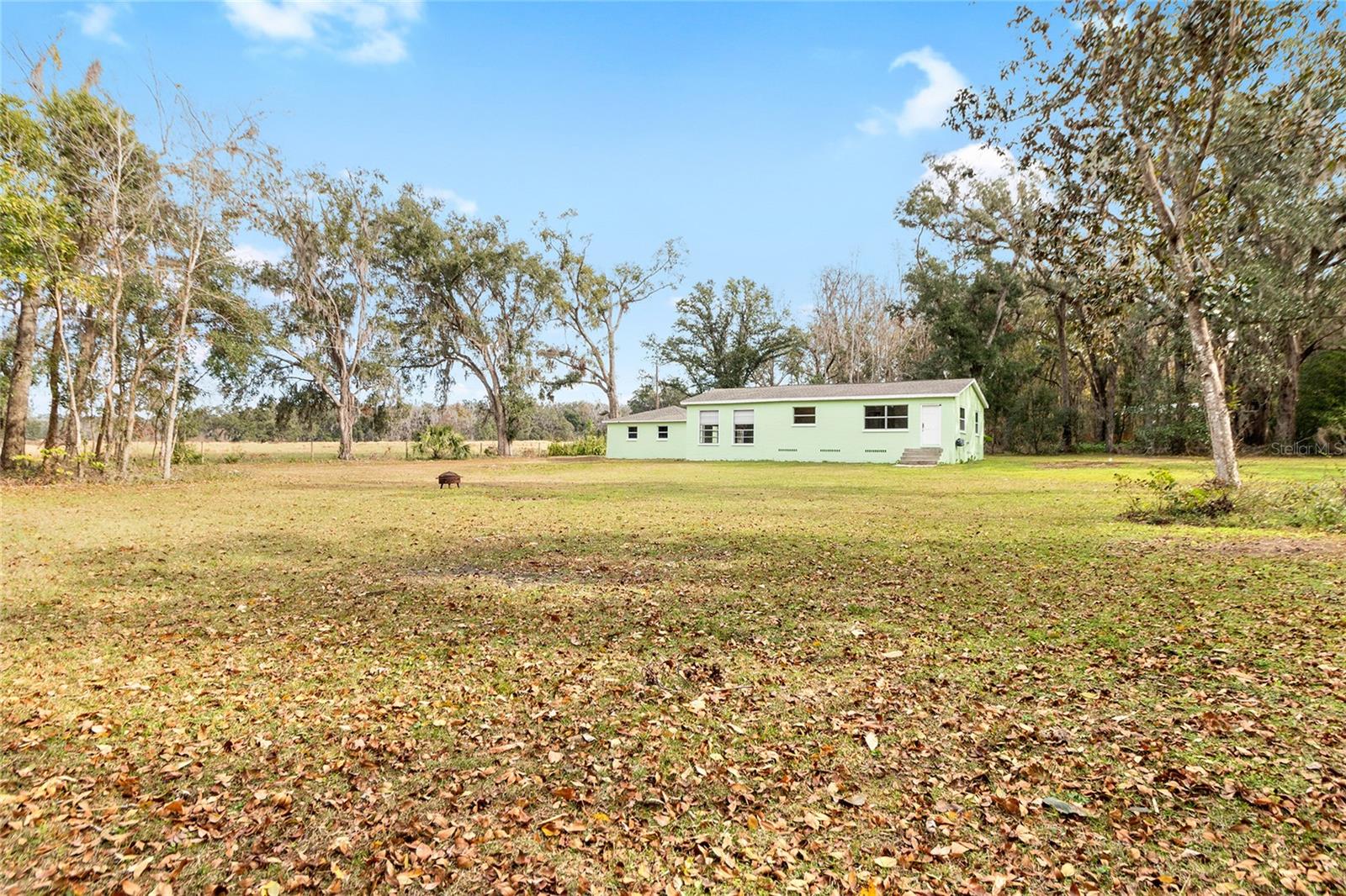 This lovely view showcases a serene 2.5 acre property with a 3/2 cement block one story home in an X flood Zone. The property includes a detached 2-car garage, a storage shed, and an RV dumpstation. The property is lined with trees for privacy. The property is surrounded by nature, and one neighbor has a vast horse and cow pasture with acres of land.