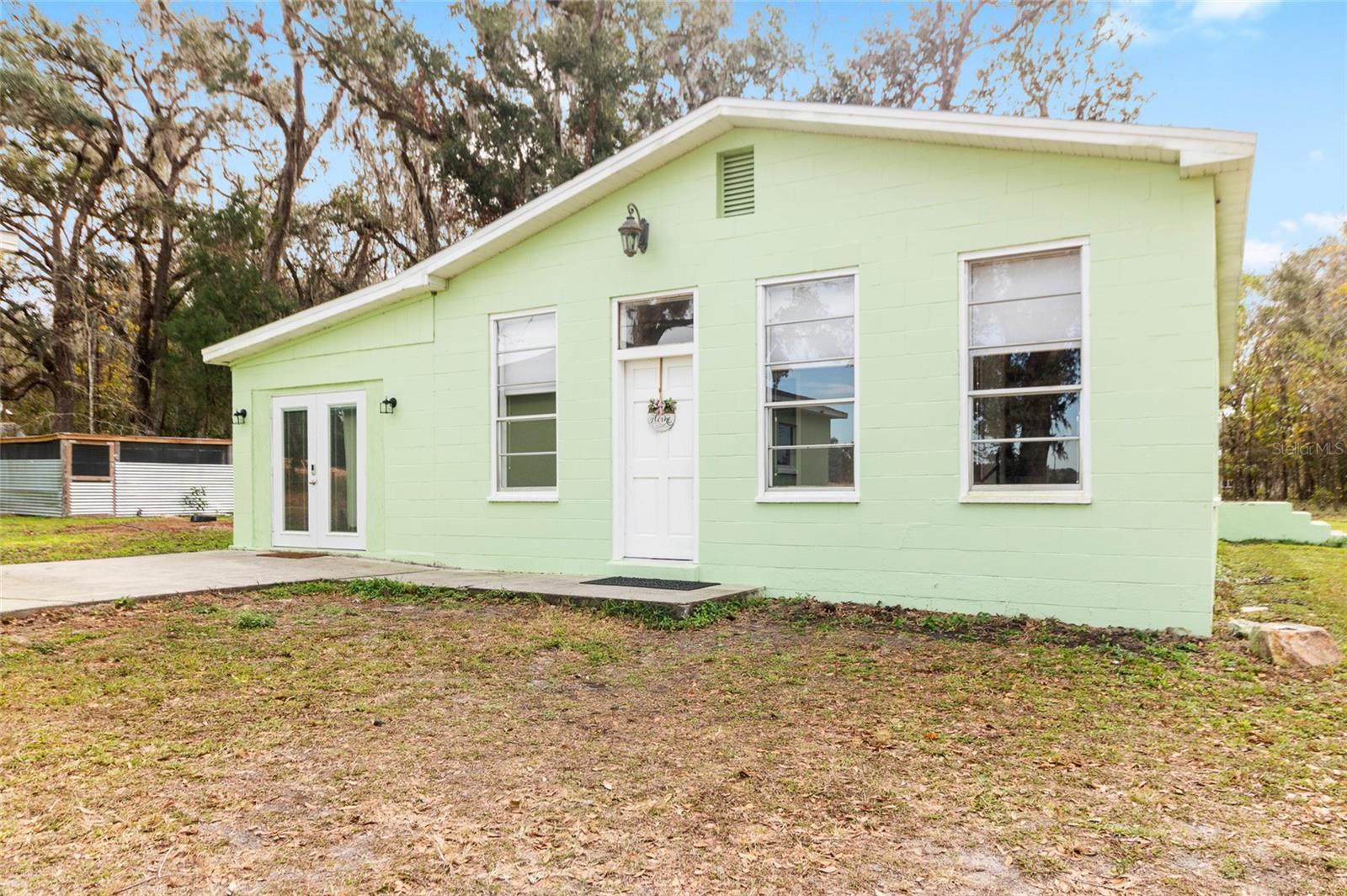 This lovely view showcases a serene 2.5 acre property with a 3/2 cement block one story home in an X flood Zone. The property includes a detached 2-car garage, a storage shed, and an RV dumpstation. The property is lined with trees for privacy. The property is surrounded by nature, and one neighbor has a vast horse and cow pasture with acres of land.