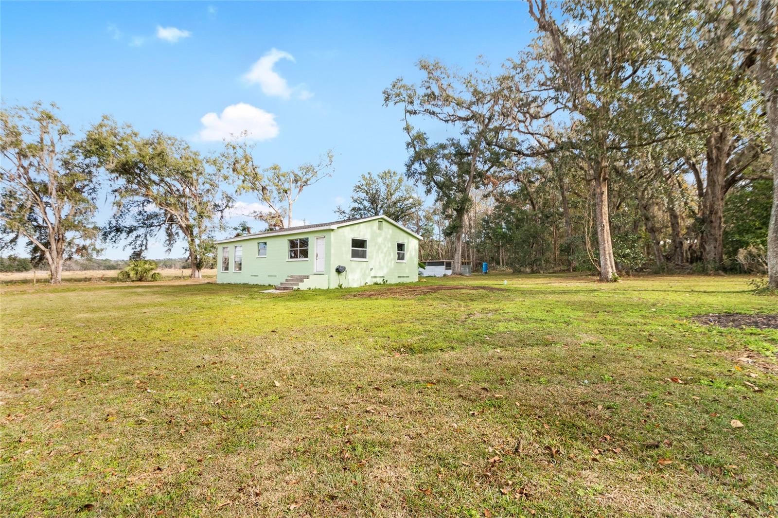 Ariel view of the serene 2.5 acre property with a 3/2 cement block one story home in an X flood Zone with a detached 2-car garage, and a storage shed, and an RV dumpstation.  Lined with trees for privacy. Surrounded by nature & one neighbor has a vast horse and cow pasture with acres of land.