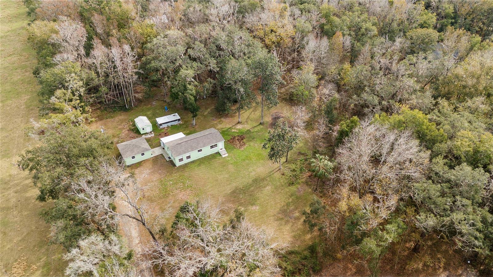 Ariel view of the serene 2.5 acre property with a 3/2 cement block one story home in an X flood Zone with a detached 2-car garage, and a storage shed, and an RV dumpstation.  Lined with trees for privacy. Surrounded by nature & one neighbor has a vast horse and cow pasture with acres of land.