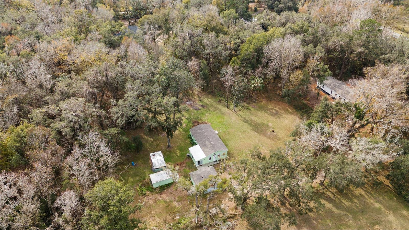 Ariel view of the serene 2.5 acre property with a 3/2 cement block one story home in an X flood Zone with a detached 2-car garage, and a storage shed, and an RV dumpstation.  Lined with trees for privacy. Surrounded by nature & one neighbor has a vast horse and cow pasture with acres of land.