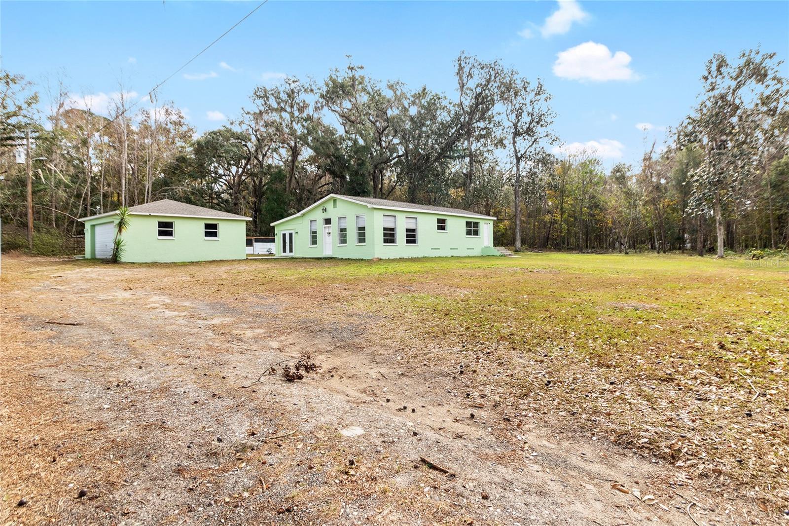 This lovely view showcases a serene 2.5 acre property with a 3/2 cement block one story home in an X flood Zone. The property includes a detached 2-car garage, a storage shed, and an RV dumpstation. The property is lined with trees for privacy. The property is surrounded by nature, and one neighbor has a vast horse and cow pasture with acres of land.