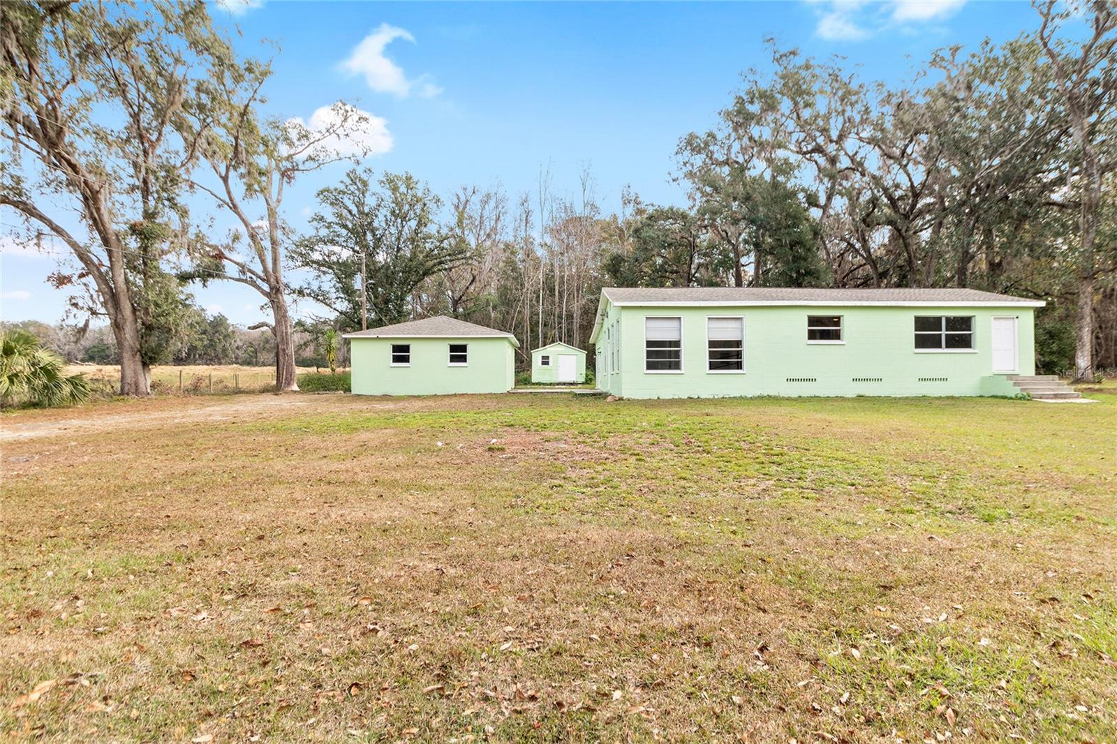 This lovely view showcases a serene 2.5 acre property with a 3/2 cement block one story home in an X flood Zone. The property includes a detached 2-car garage, a storage shed, and an RV dumpstation. The property is lined with trees for privacy. The property is surrounded by nature, and one neighbor has a vast horse and cow pasture with acres of land.