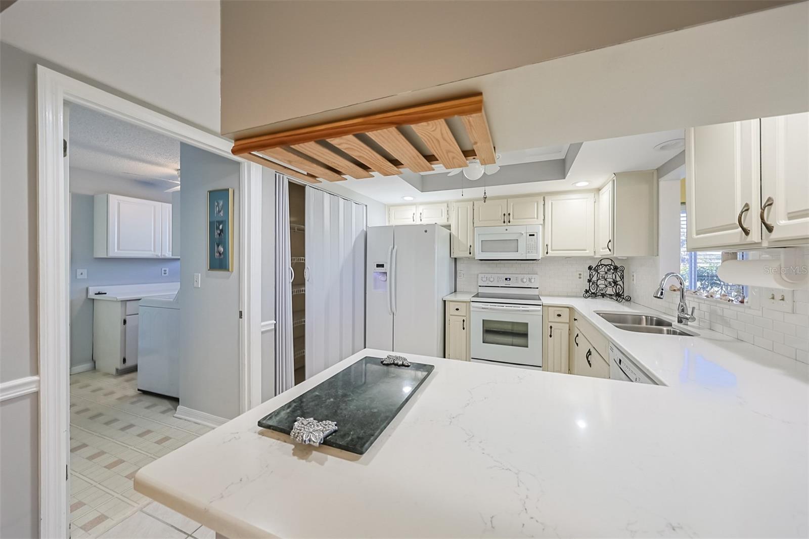 Kitchen allows for multiple cooks and is well equipped with dishes, cooking utensils, etc.  The view from the kitchen sink ensures that you never feel 'enclosed'.  Notice the kitchen also connects to the large separate indoor laundry room. Includes a wine rack and is lined with a subway tile backsplash. Recessed lighting adds for additional brightness. Includes pantry and undermount sink overlooking the Florida room.