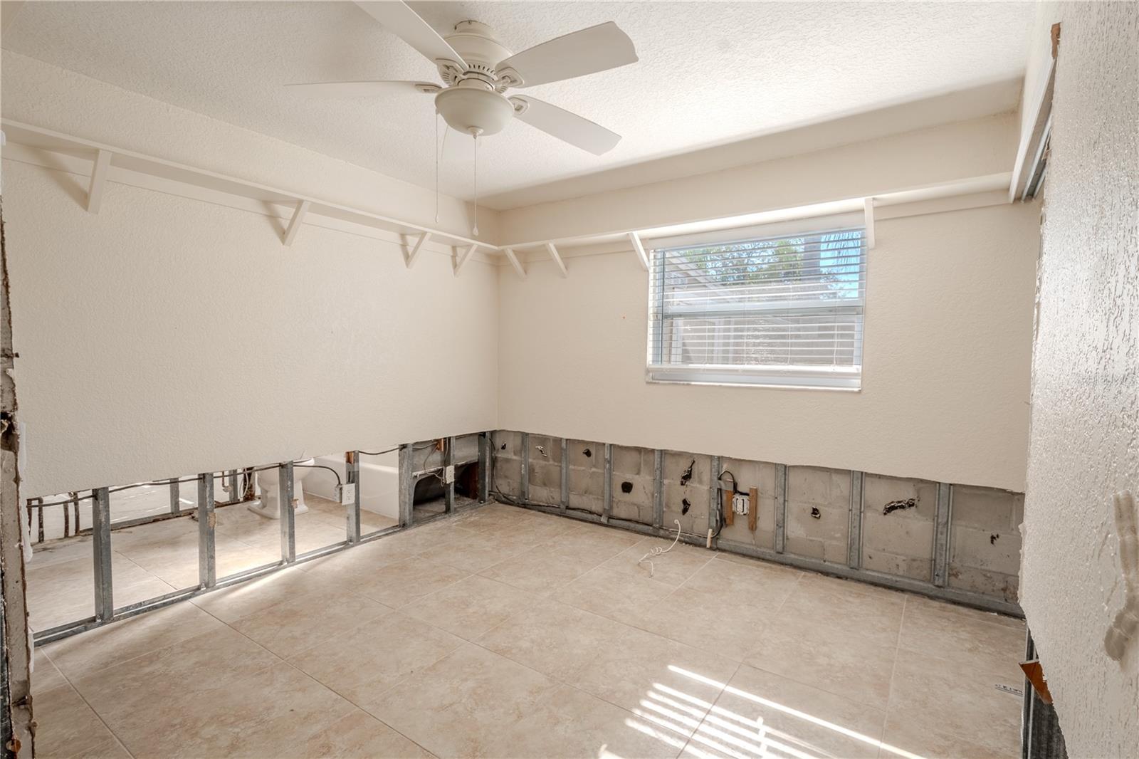 3rd bedroom has a tiled floor, ceiling fan and display shelf.