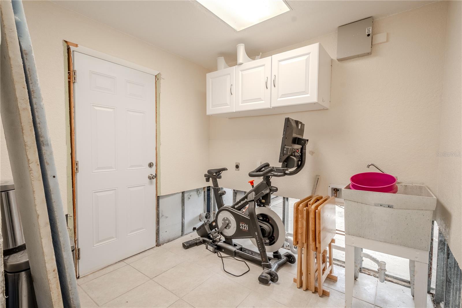 Laundry room has a tile floor and overhead cabinets.