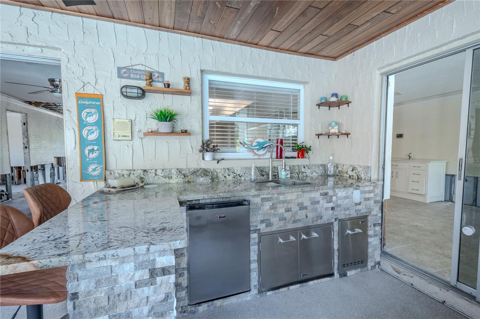 The outdoor kitchen features a stainless steel refrigerator and stainless steel sink