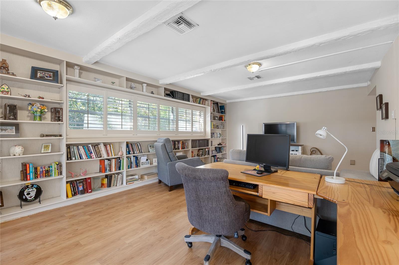 The living room exudes charm with its beamed ceilings, built-in bookcases, and elegant plantation shutters, creating a warm and inviting atmosphere