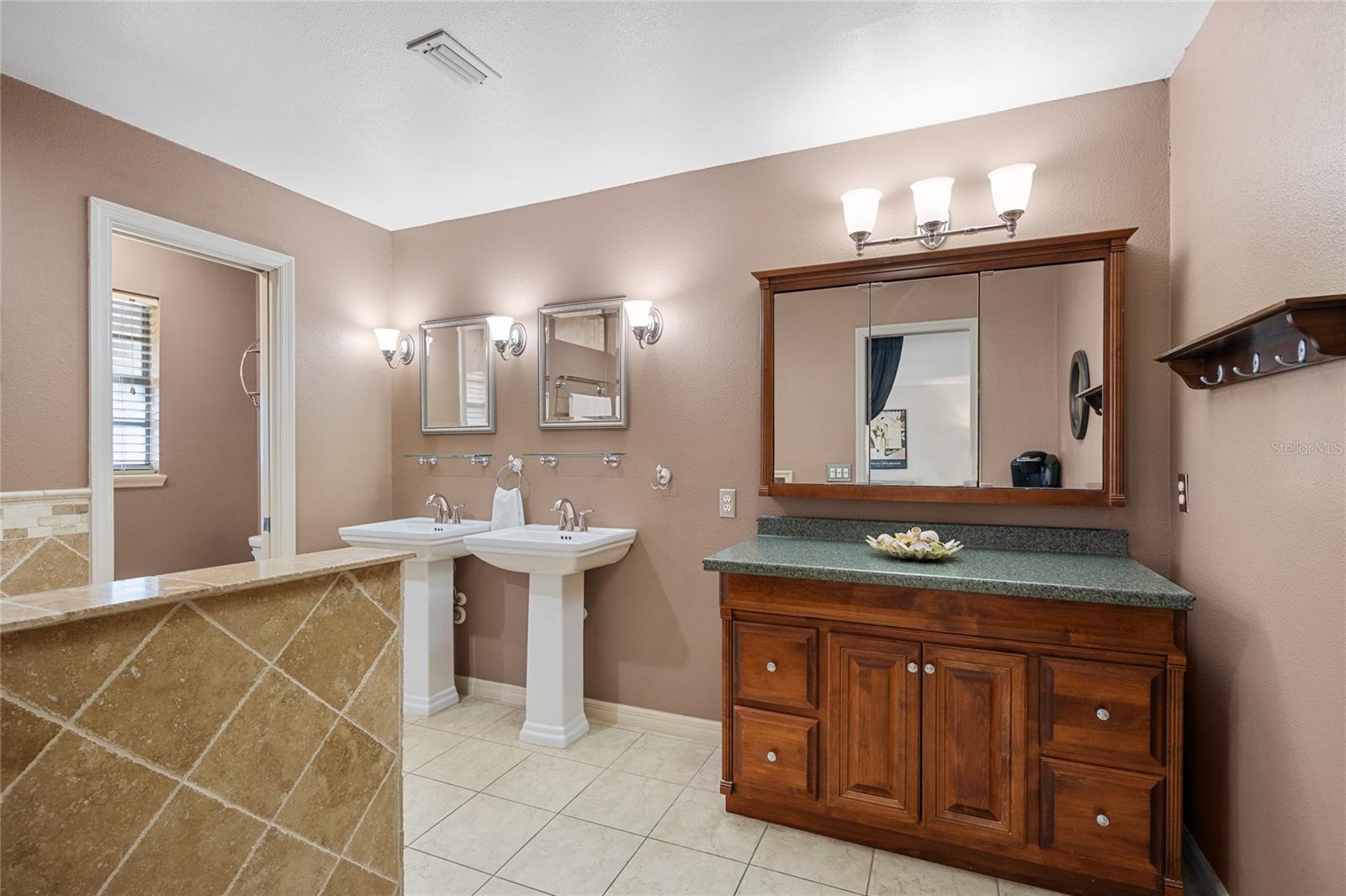 The owner's suite bathroom features a private water closet and shower area, along with a luxurious jetted tub, double pedestal sinks, and a separate makeup counter, creating a spa-like retreat.