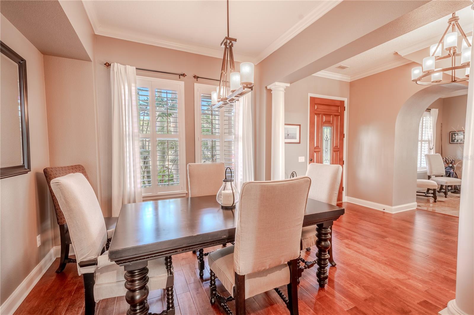 The Dining room features a neutral color palette, wood floors,  crown molding and chandelier, and a picture window with wood shutters.