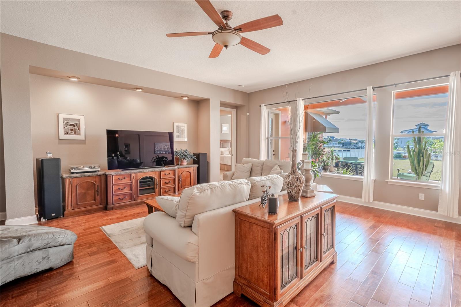 The living/family room is bathed in warm tones with wood floors, high ceiling and a ceiling fan.