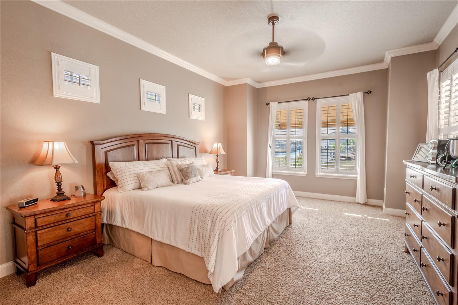 The Primary bedroom is located on the first floor and features warm hues, crown molding, port accent windows, wood shutters, plush carpet, a ceiling fan for year round comfort, and an ensuite bath.