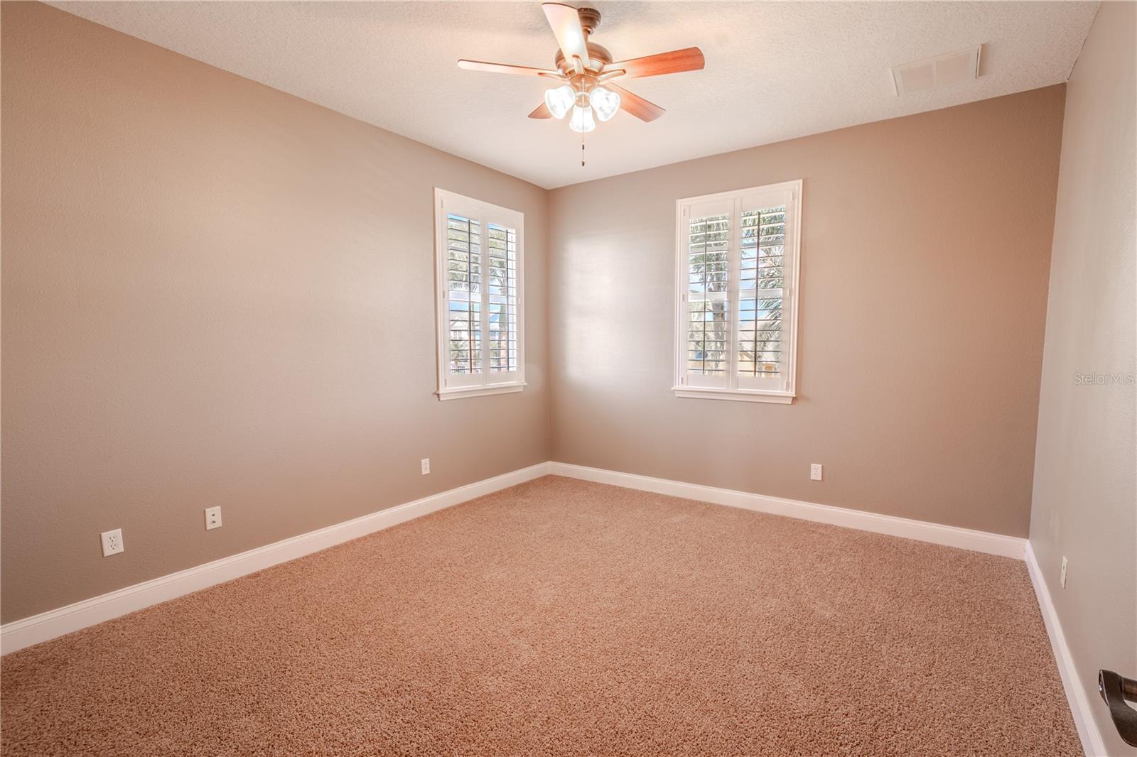 Bedroom 4 features warm tones, wood shutters, a built-in closet, a ceiling fan and plush carpet.