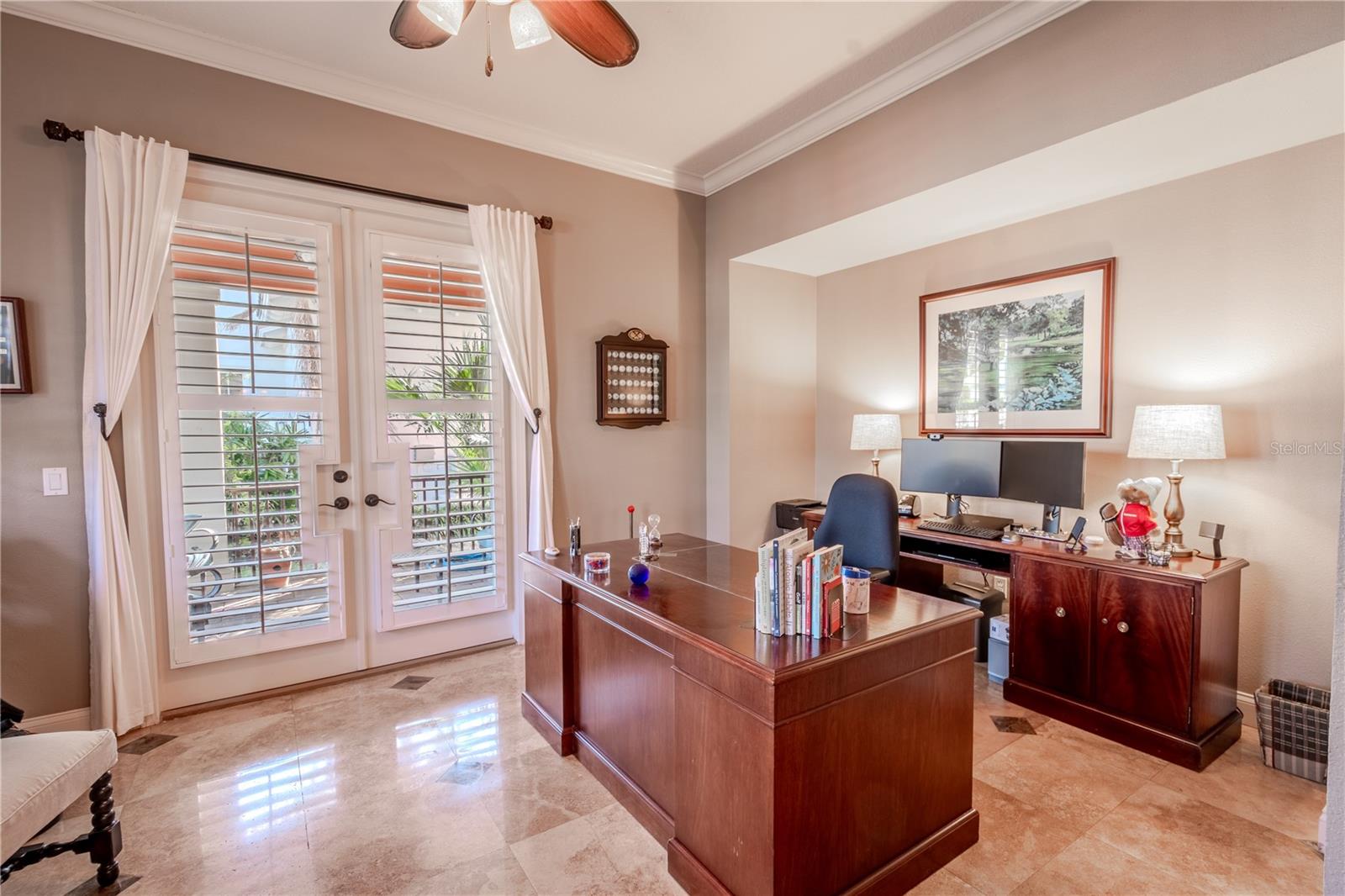 The home office features neutral tones, stylish marble flooring, crown molding, a built in closet and French Doors that lead to a covered patio.