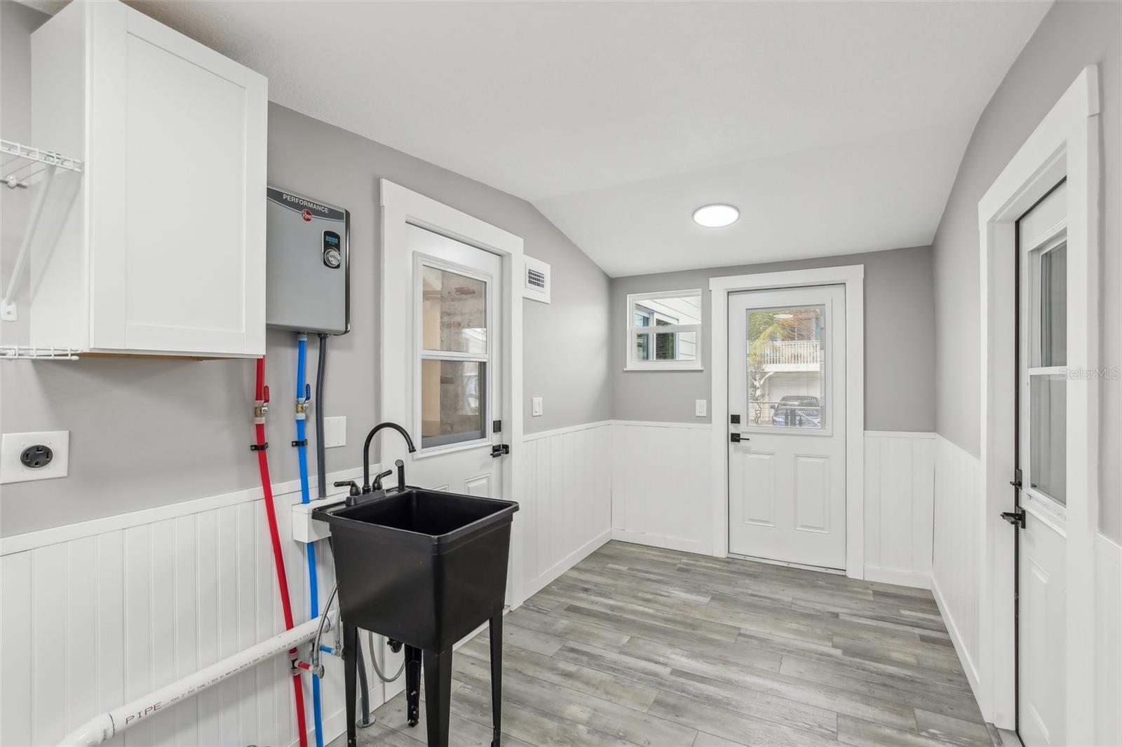 Mud Room with washer and dryer hookup, sink, storage cabinet, and your new tankless hot water heater.