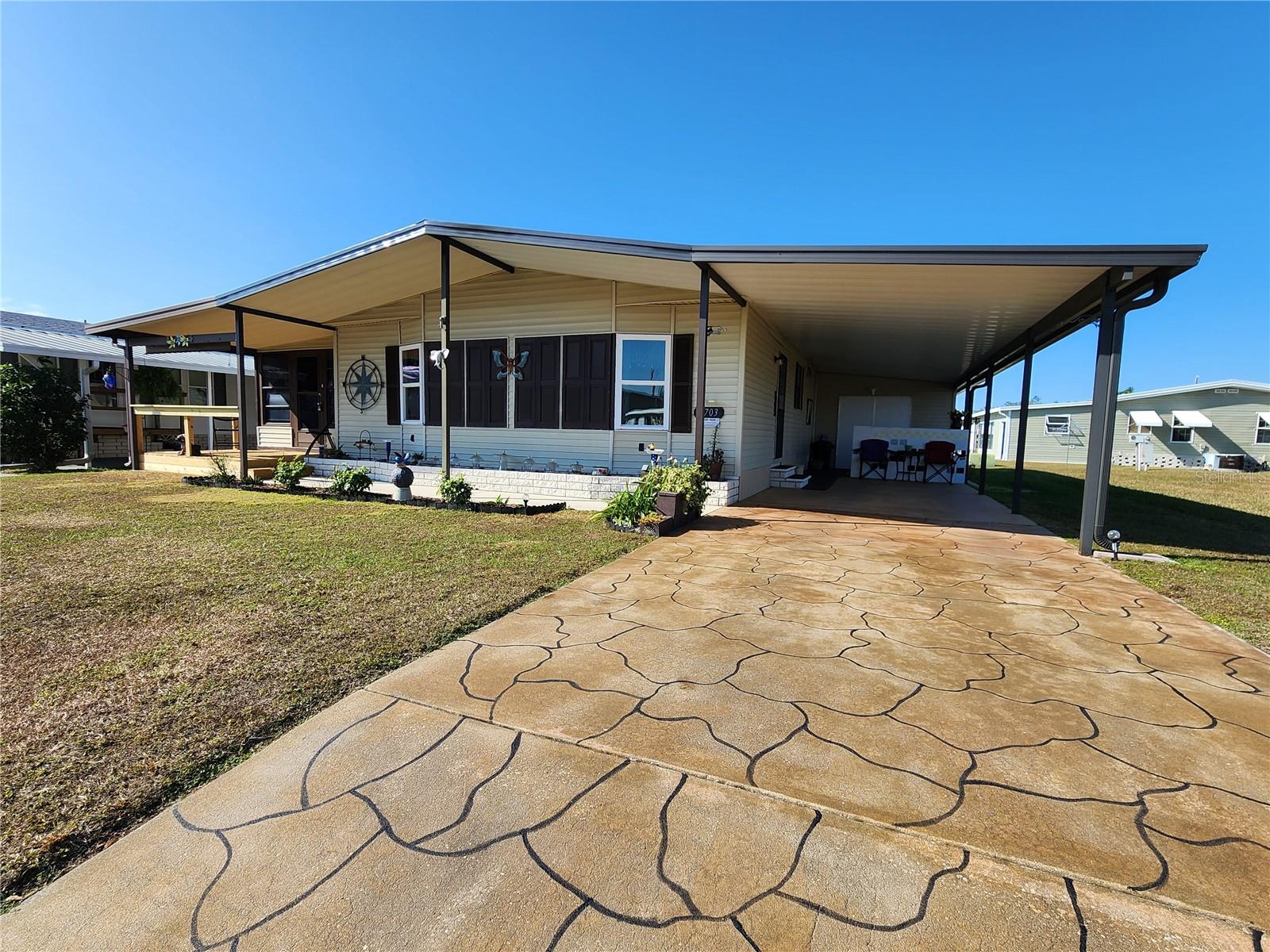 Front, East facing. Decorative painted driveway. Carport & wide front overhang with sidewalk & planter.