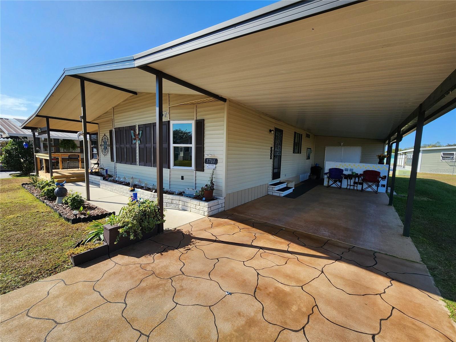 Front, East facing. Decorative painted driveway. Carport & wide front overhang with sidewalk & planter.