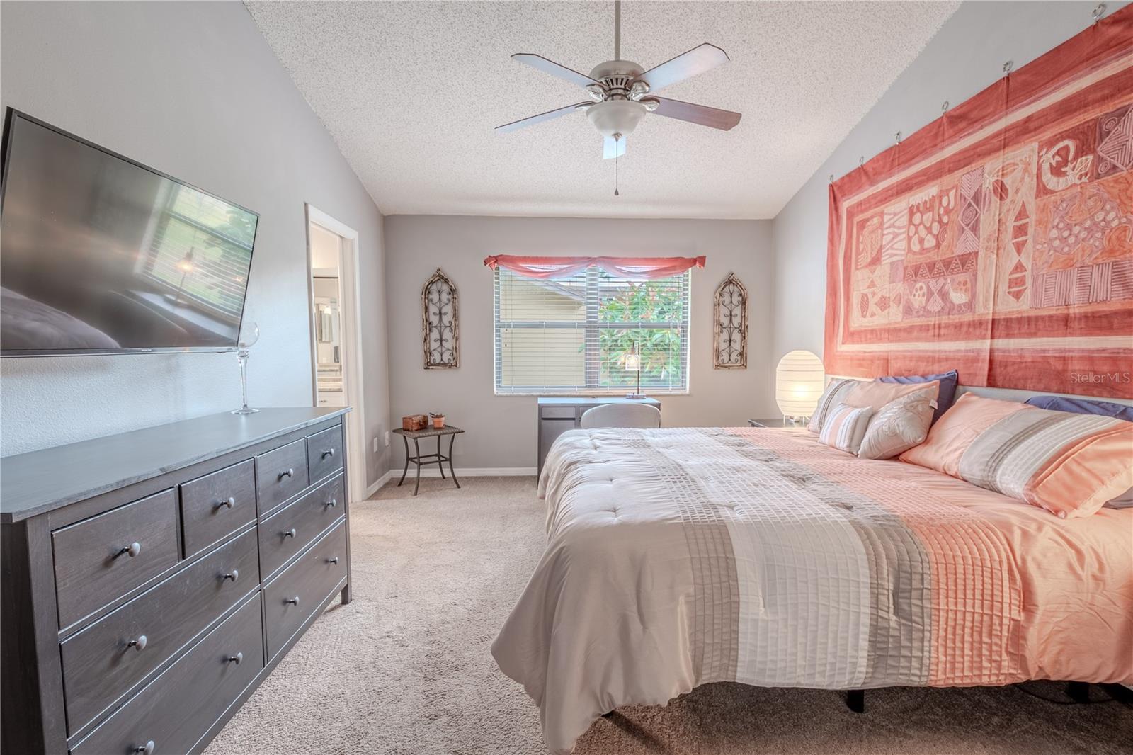 The primary bedroom features plush carpet, a walk-in closet, a ceiling fan with light kit and a vaulted ceiling.