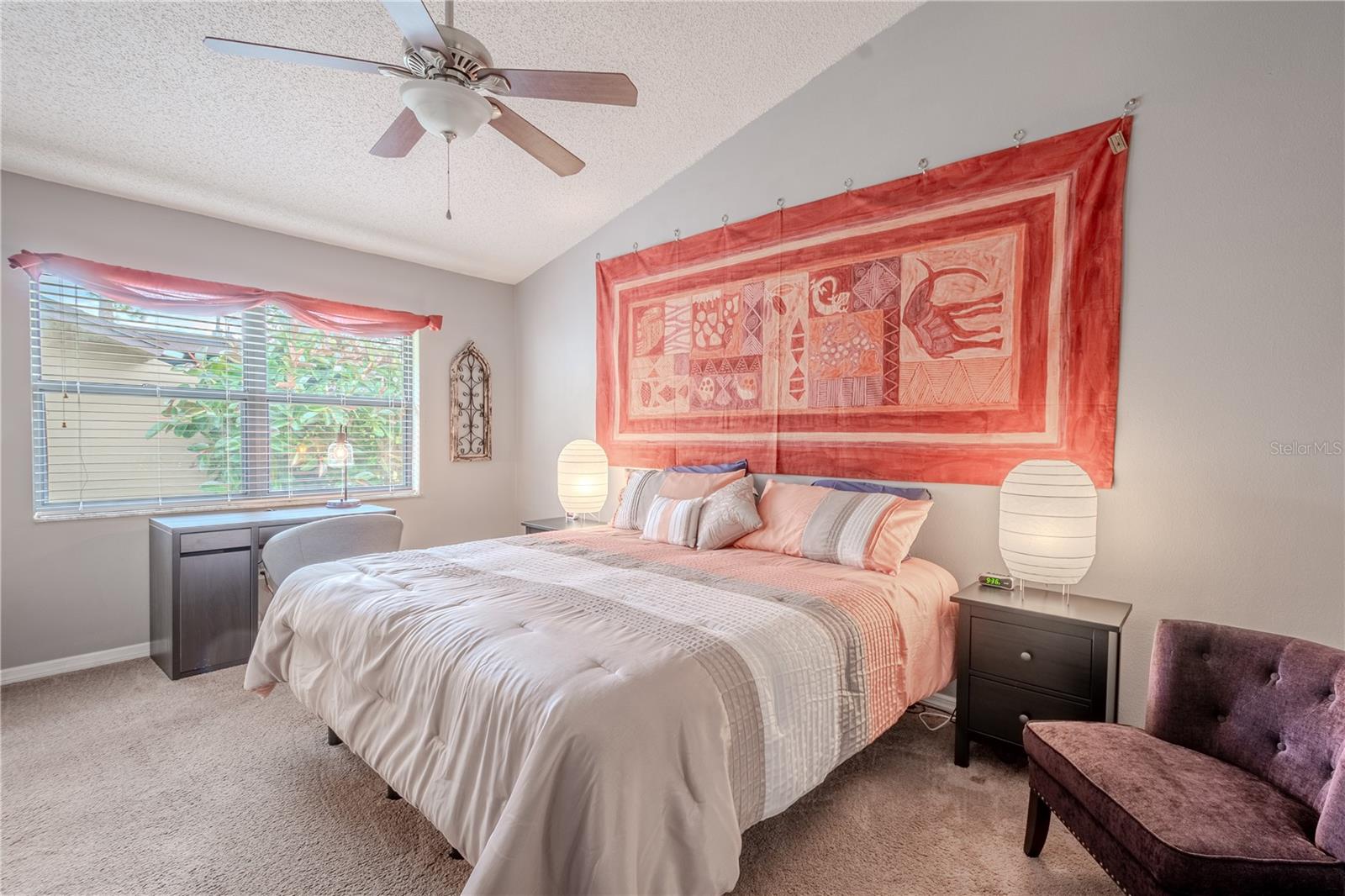 The primary bedroom features plush carpet, a ceiling fan with light kit and a vaulted ceiling.