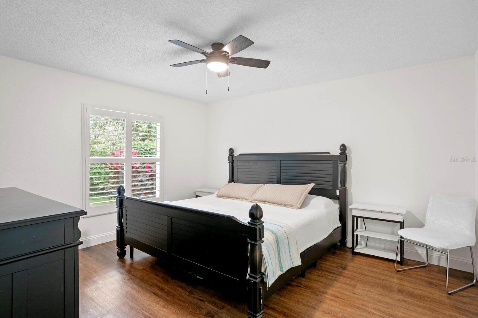 Large primary bedroom with ceiling fan and backyard views