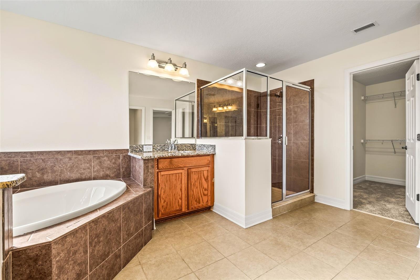 Ensuite owners bathroom featuring tub, walk in shower, split vanities, and two walk in closets.