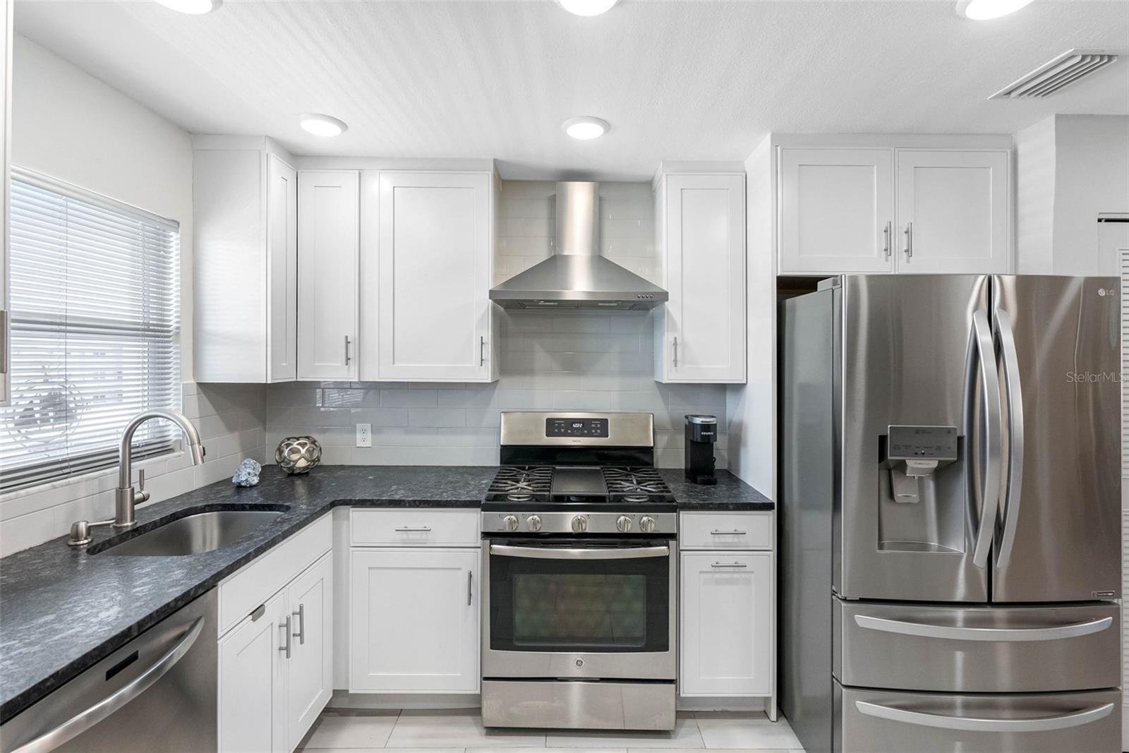 A remodeled kitchen with leathered granite countertops, stainless steel appliances, and a gas stove.