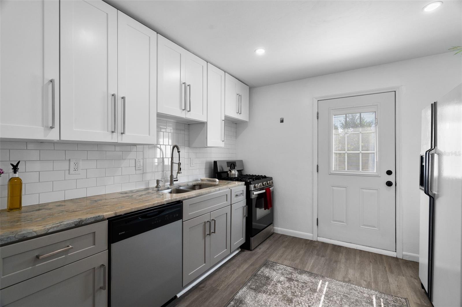 Kitchen showcases stylish tuxedo cabinetry, luxury vinyl plank flooring, stone countertops, chic tile work, and a gas stove.