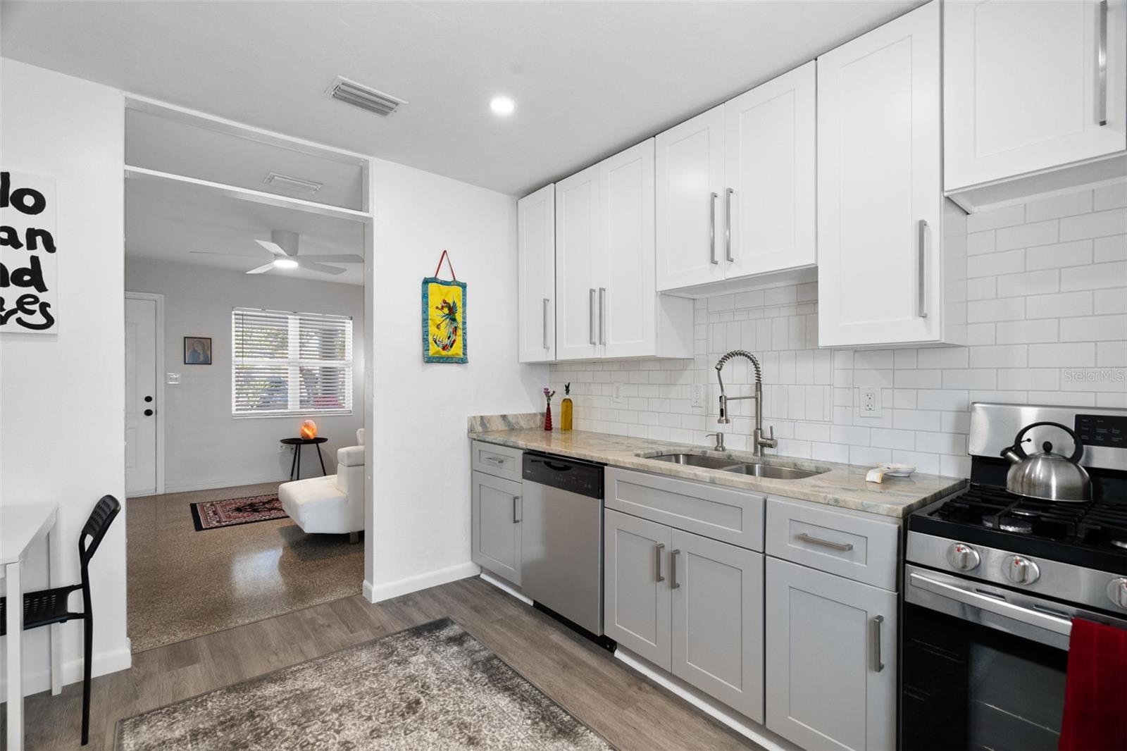 Kitchen showcases stylish tuxedo cabinetry, luxury vinyl plank flooring, stone countertops, chic tile work, and a gas stove.