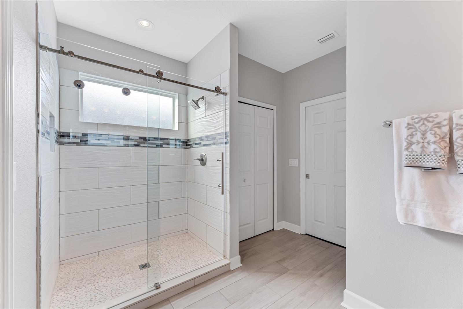 The spa-like en suite bathroom featuring a massive shower with sliding glass barn doors and a pebble tile shower base.