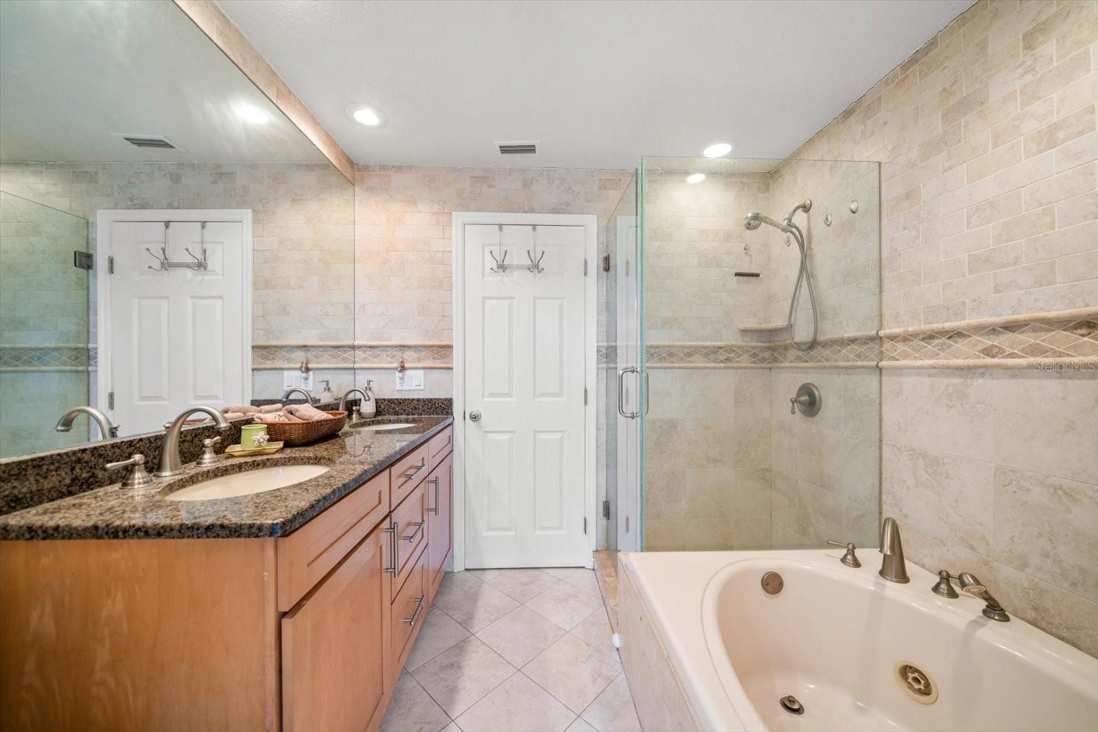 Spa-like bathroom featuring well-crafted stone work, glass shower door, and jetted tub.