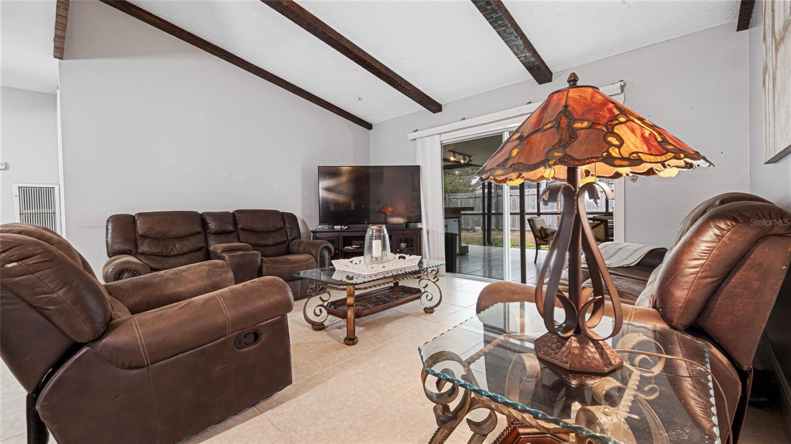 Inviting family room with an open layout, vaulted ceilings, exposed wood beams, and a dual-sided brick fireplace.Sliding doors lead to a screened patio.