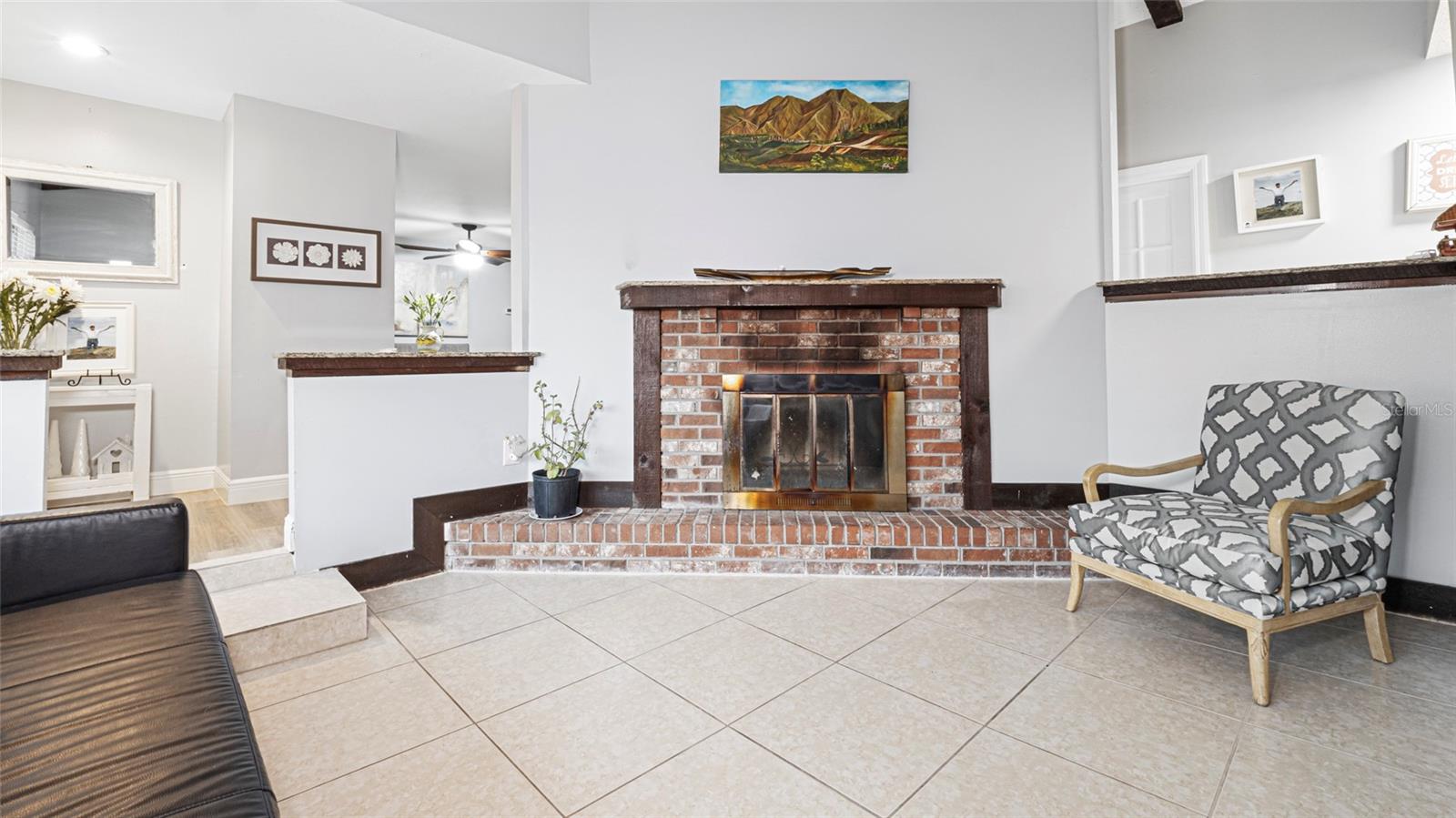 Formal living room boasts soaring high ceilings and a wood-burning brick fireplace as the focal point, offering warmth and charm. The fireplace is dual-sided, connecting this space with the adjacent family room.