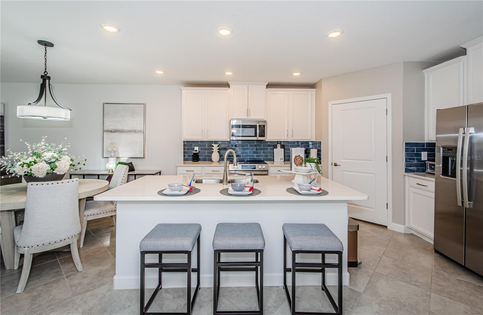 Elevate your culinary experience in this modern gourmet kitchen, where style and function blend seamlessly. Crisp white shaker cabinets, quartz countertops, and a bold blue tile backsplash create an inviting space that feels both contemporary and timeless. The stainless-steel appliances gleam under recessed lighting, making meal preparation a joy. With ample storage, a large island with bar seating, and a walk-in pantry, this kitchen is designed for both casual dining and entertaining. Let the heart of your home inspire your next culinary masterpiece.