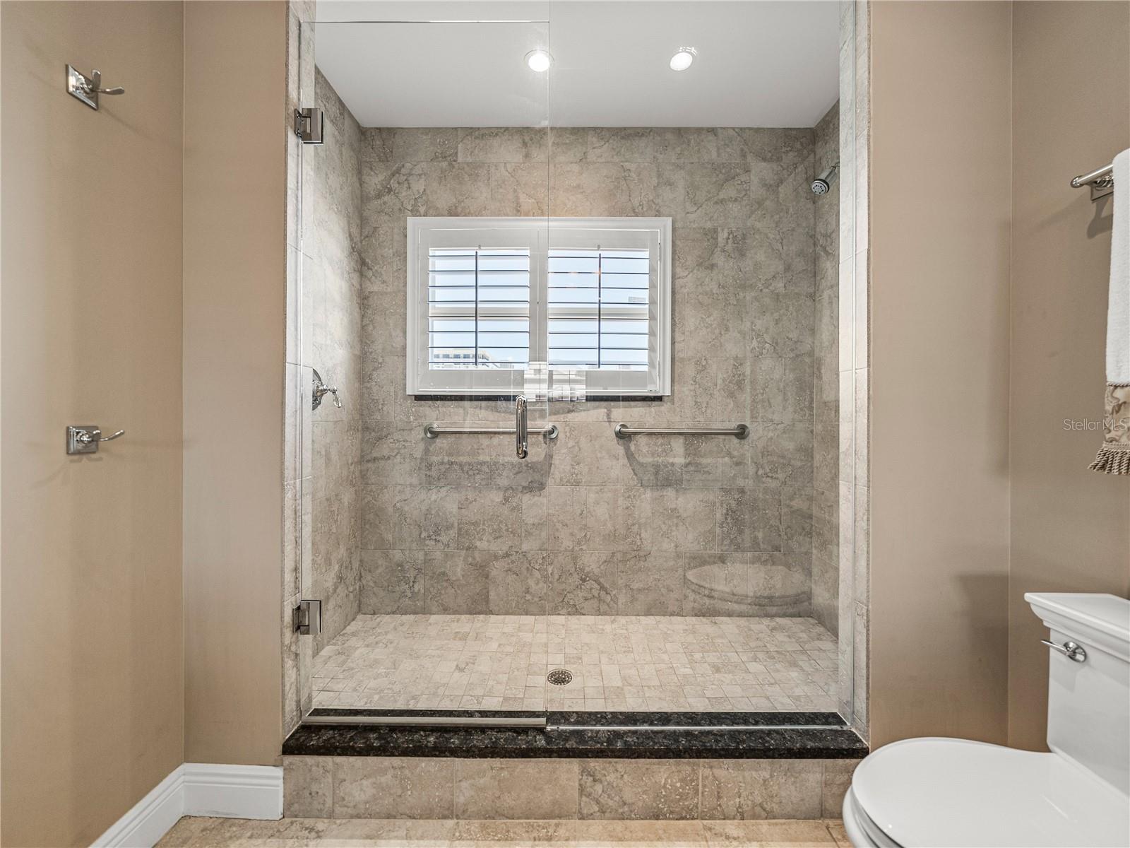 The spacious shower has porcelain tile and a frameless glass enclosure.