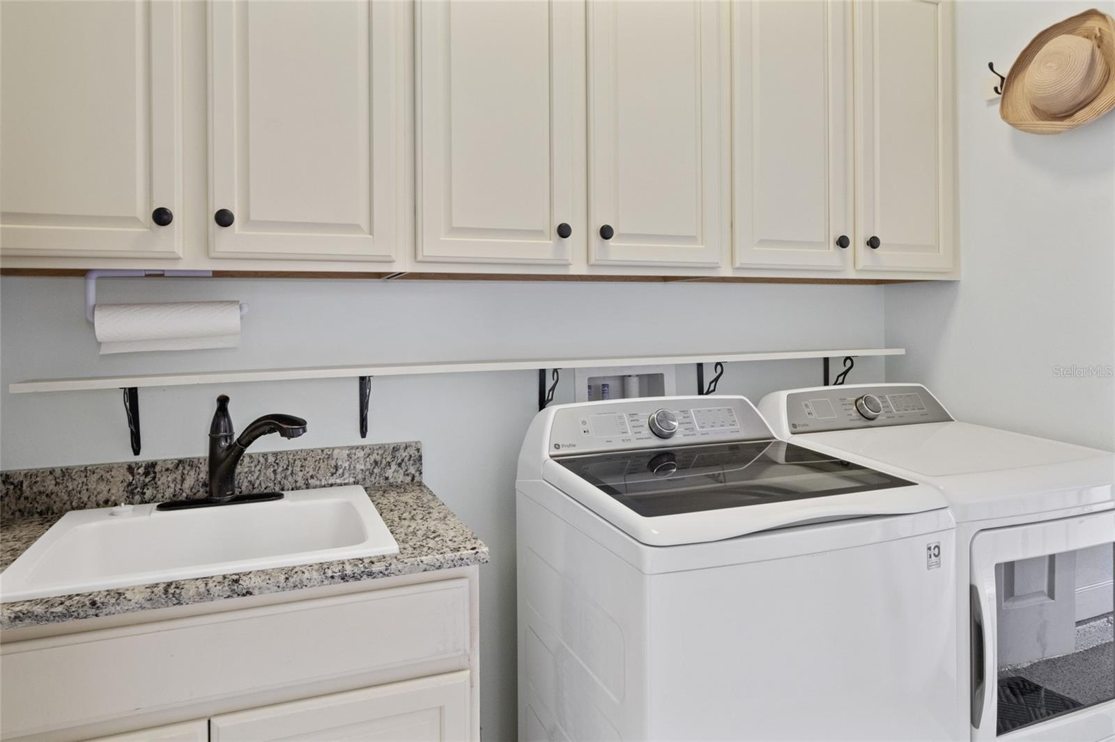 Inside laundry room off of garage with granite counter utility sink and plenty of storage cabinets, shelving & hooks