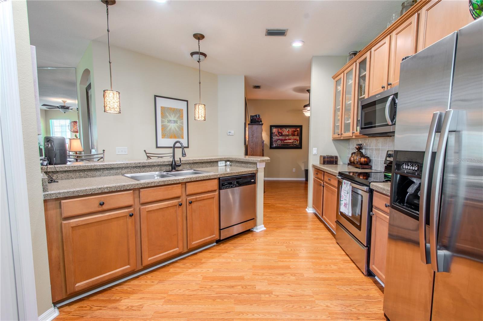 The kitchen features a breakfast bar with stylish pendant lights, recessed lighting, wood laminate flooring, and solid wood cabinetry.