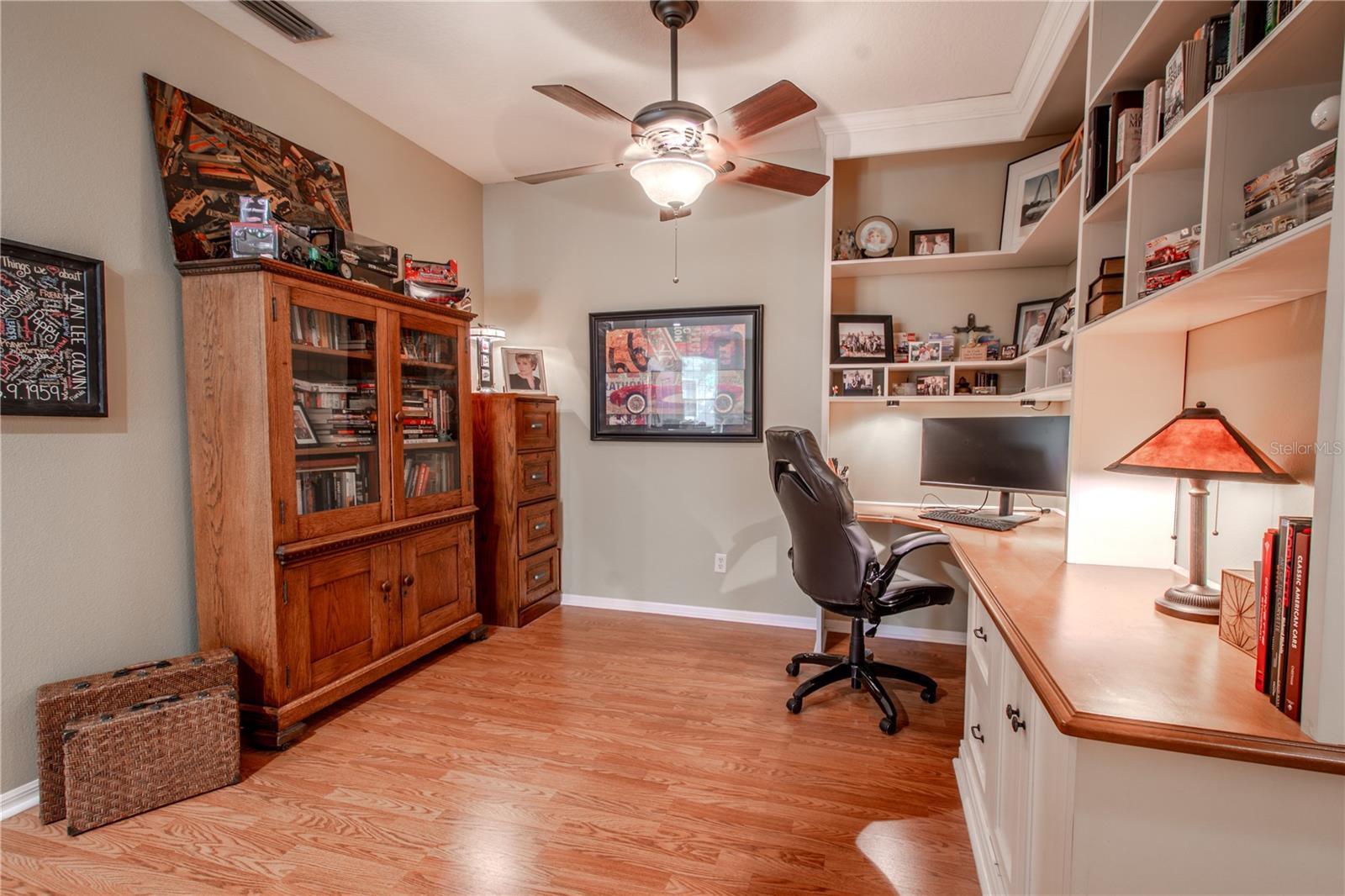 The office features a ceiling fan with light lit, neutral tones and a wood laminate floor.