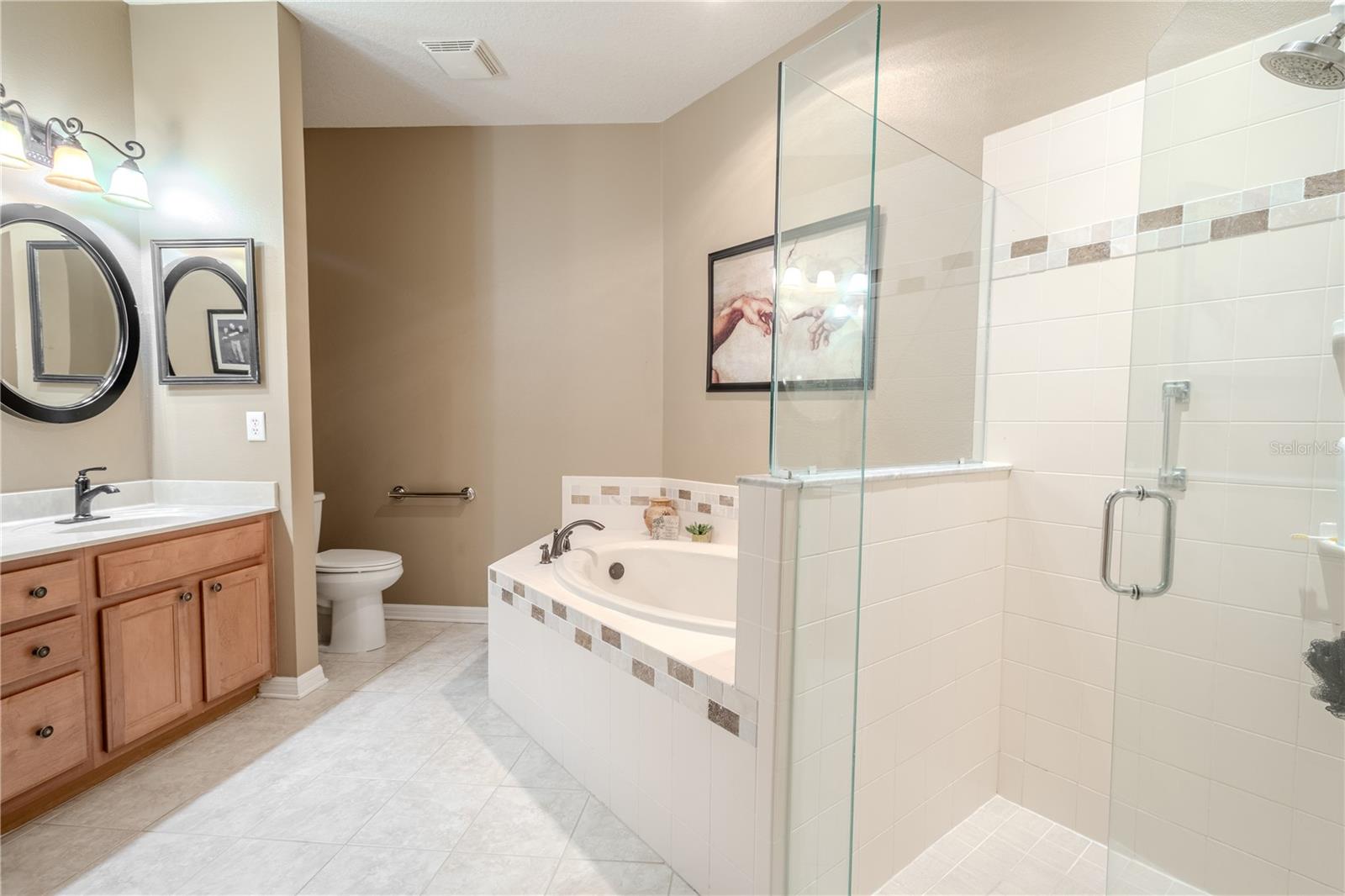 The primary ensuite features a garden tub, a glass enclosed shower, a mirrored, dual sink wood vanity with down light fixtures.