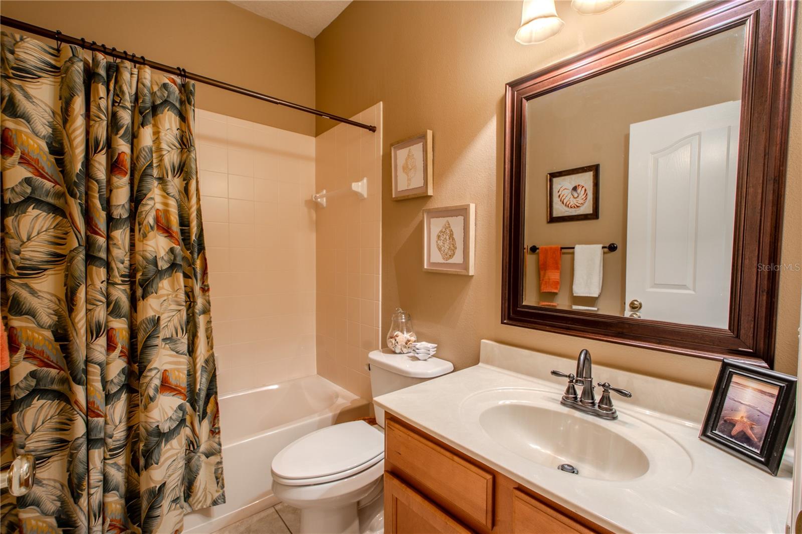 Bathroom 2 features a mirrored wood vanity with storage, ceramic tile floor and a tub with shower.