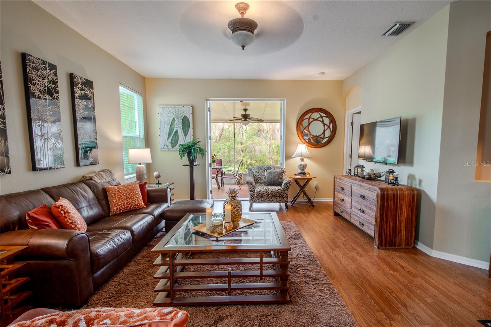 The living room features wood laminate flooring, neutral tones and a ceiling fan. French doors open from the living room to the lanai.