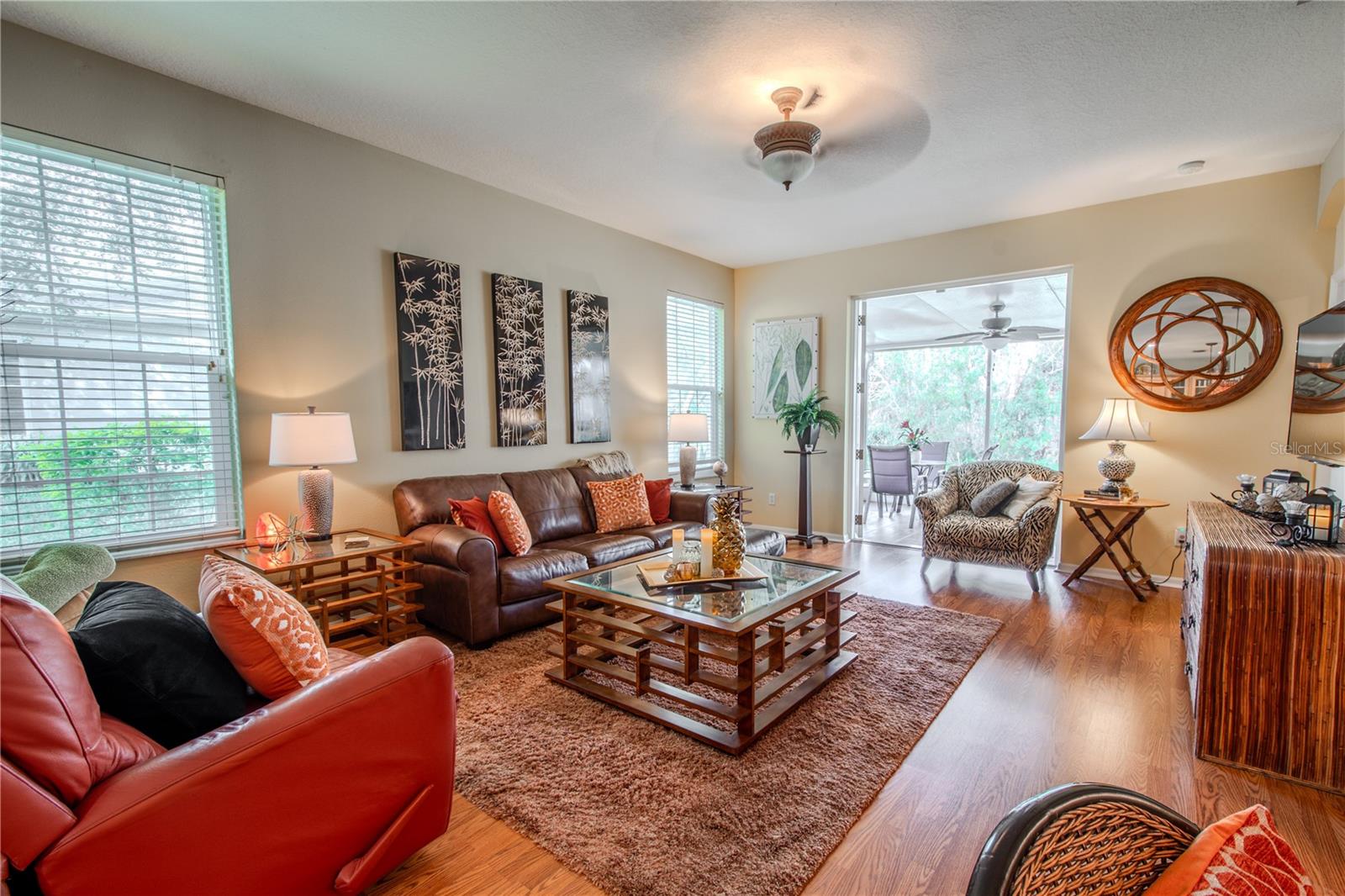 The living room features wood laminate flooring, neutral tones and a ceiling fan. French doors open from the living room to the lanai.